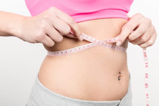 A young woman with a baunch navel piercing measures her waist with a band of measure