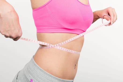 A young woman with a baunch navel piercing measures her waist with a band of measure