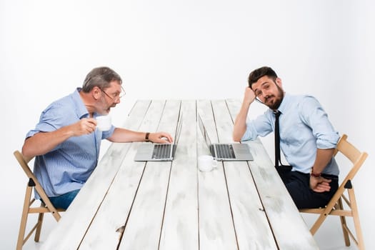 The two colleagues working together at office on light gray background. one  smiling man is satisfied, another man in stress looking at the computer screen.  the concept of competition in the business