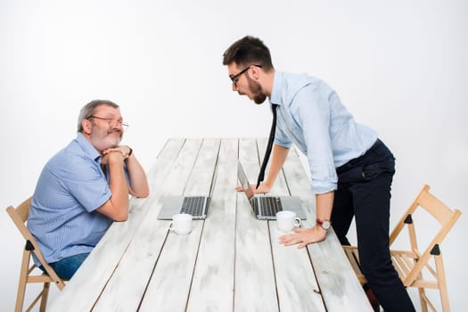 The two colleagues working together at office on light gray background. one  smiling man is satisfied, another indignant.  the concept of competition in the business