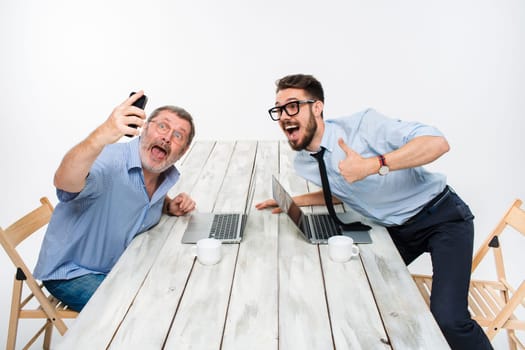 Two colleagues taking the picture to them self sitting in the office, surprised friends with glasses taking selfie with telephone camera  on white background