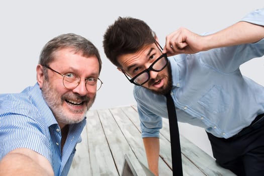 Two smiling colleagues taking the picture to them self sitting in the office, happy friends with glasses taking selfie with telephone camera  on white background