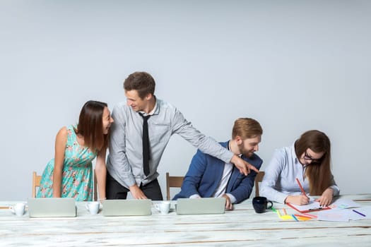 Business team working on their business project together at office on light gray background.  all smiling and looking at the boss. the boss is writing in a notebook. copyspace image.