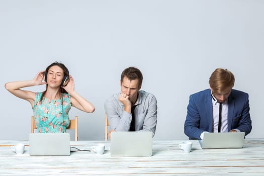 Business team working together at office on light gray background. all working on laptops. girl in headphones enjoying the music