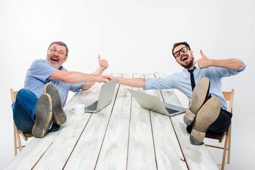 The two smiling businessmen with legs over table holding hands on white background. Business in the American style - concept understanding and success