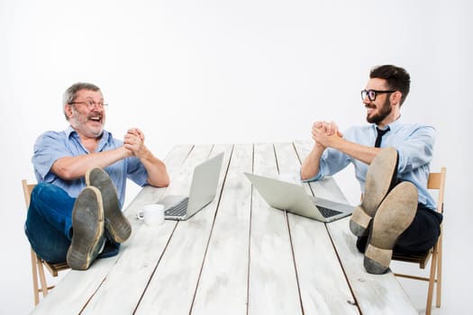 The two smiling businessmen with legs over table working on laptops on white background. Business in the American style - concept understanding