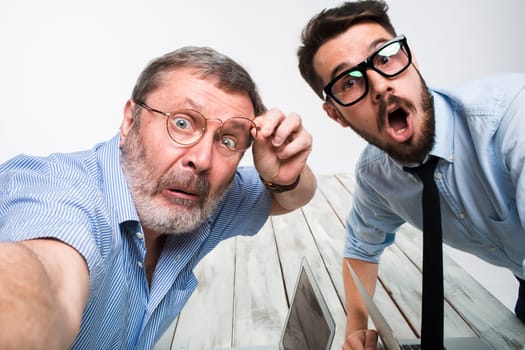 Two colleagues taking the picture to them self sitting in the office, surprised friends with glasses taking selfie with telephone camera  on white background