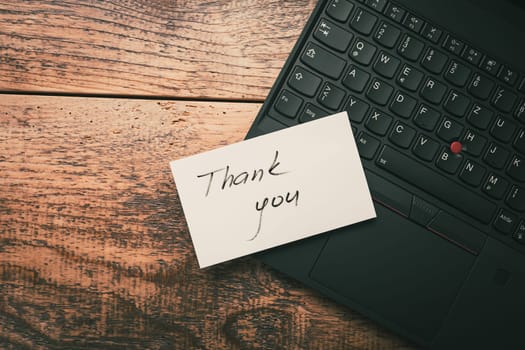 Closeup of Thank You sticky note message on laptop on wooden background