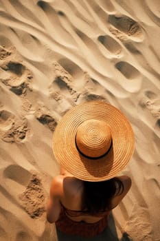 Fashionable young woman in a fashion straw hat in a vintage swimsuit sits and relaxes on the sand on the beach near the sea on a sunny day, top view