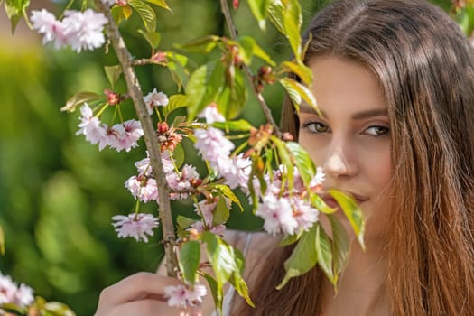 Attractive brunette girl posing on camera partially covered by a sprig of cherry blossoms. Horizontally.