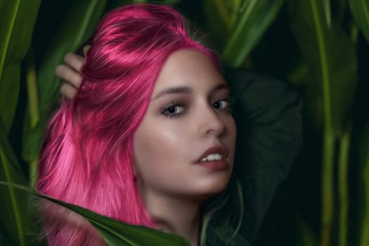 Young pink hair woman poses among the green plants. Horizontally.