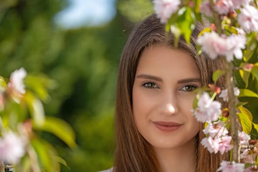 Attractive brunette girl posing near sprig of cherry blossoms. Horizontally.