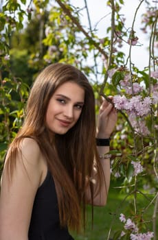 Attractive brunette girl dressed in a black dress is holding a sprig of cherry blossom. Vertically.