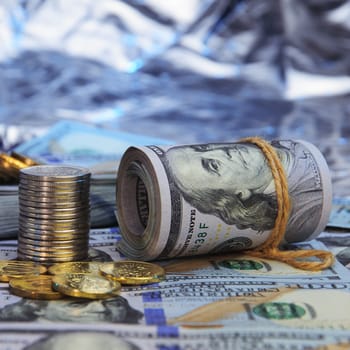 Stacks of coins against the background of hundred-dollar bills are scattered throughout the space. The coins are shiny, golden in color.