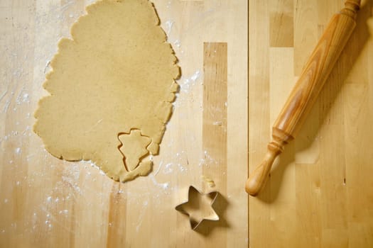 Top view of kitchen table with rolled out cookie dough, metal cutter and wooden rolling pin