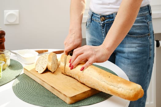 Closeup view of female hands cutting fresh baguette on slices
