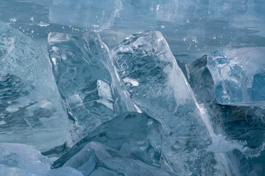 Transparent blue ice floes piled in ice hummocks against a blue sky on a sunny day. Unusual winter landscape of the frozen lake Baikal. Natural cold background. Siberia, Russia.
