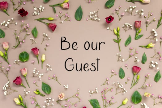 Flower Arrangement With English Text Be Our Guest. Colorful Spring Blossoms And Flowers Like Roses Building A Frame. Flat Lay With Brown Paper Background