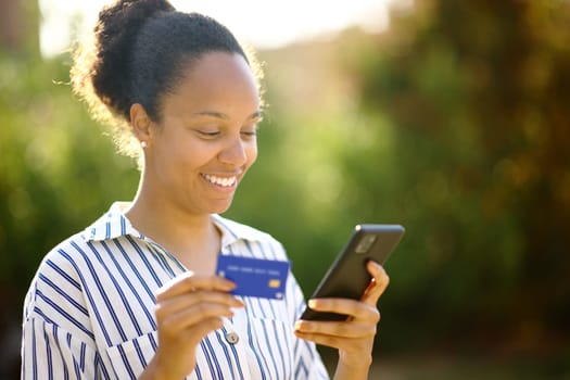 Black woman buying online with credit card and smart phone in a park