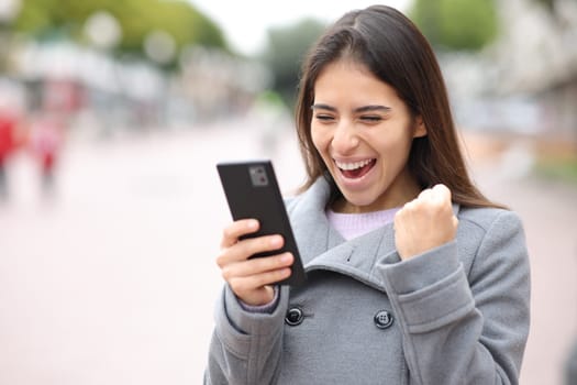 Excited woman checking content on phone in the street