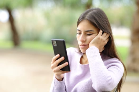 Bored woman checks smart phone sitting in a park