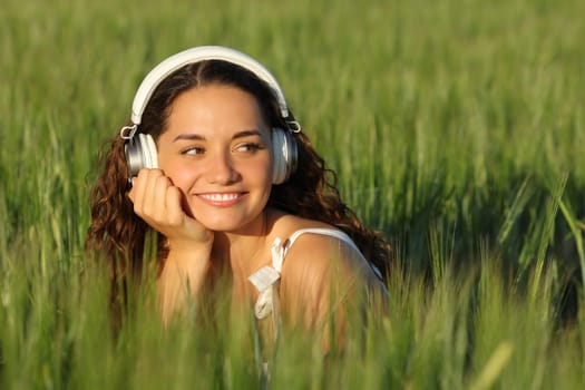 Happy woman listening to music in a green field looking at side
