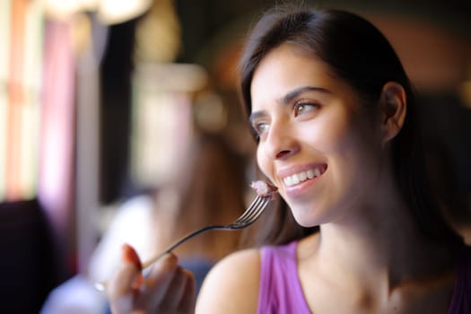 Happy woman eating meat in a restaurant looking away