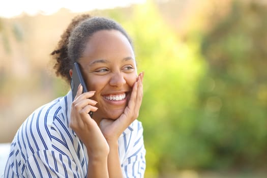 Happy candid black woman calling on phone in a park