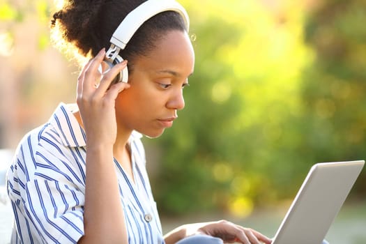 Serious black woman wearing headphone watching video on laptop in a park