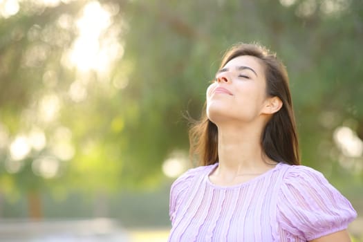 Satisfied woman breathing fresh air in a park standing alone