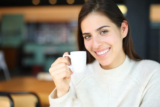 Happy woman smiling holding coffee cup in a bar looking at camera