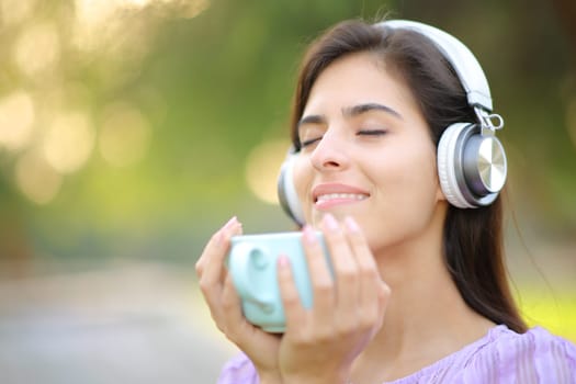 Relaxed woman wearing headphone listening music and drinking coffee in a park