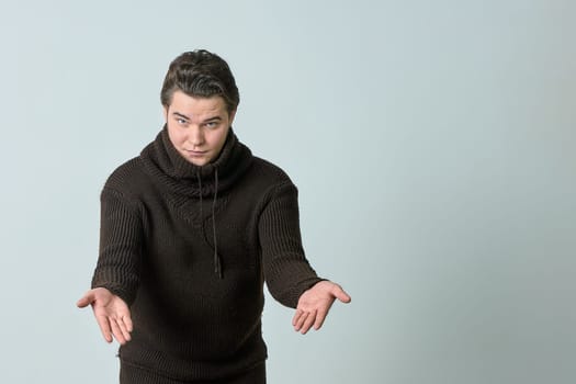 A man on a gray background in a brown sweater showing emotions, shows his hands. High quality photo