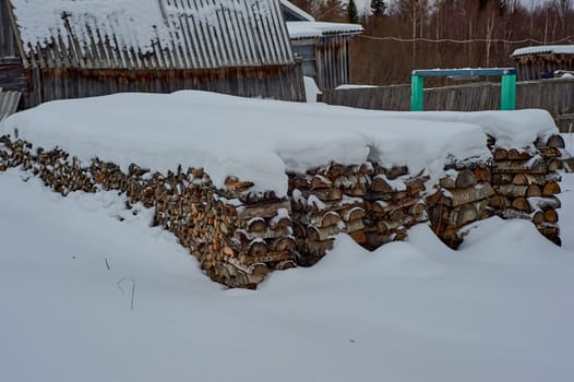 Birch split firewood stacked in a bonfire lying under the snow. High quality photo