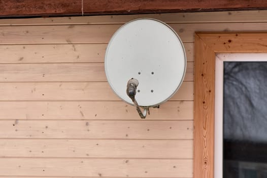 A satellite dish is hanging on the wall of a wooden house. High quality photo