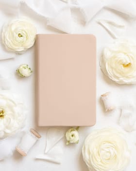 Cream hardcover textbook near cream roses and white silk ribbons top view, mockup. Romantic scene with notebook and pastel flowers. Valentines, Spring or Mothers day concept