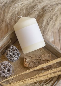Candle with blank paper label on wooden tray near dried pampas grass and natural decor, Close up, copy space. Boho packaging mock up. Home decorations, Bohemian or scandinavian style