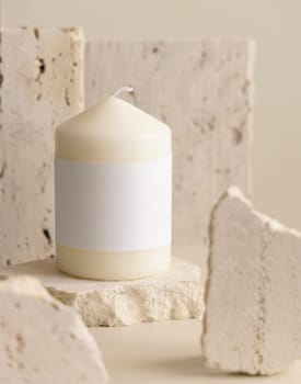 Candle with label on beige near cream travertine stones, Close up, copy space. Brand packaging mock up. Home decoration, minimal interior, Bohemian or scandinavian style