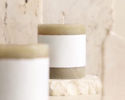Candles with label on beige near cream travertine stones, Close up, copy space. Brand packaging mock up. Home decoration, minimal interior, Bohemian or scandinavian style
