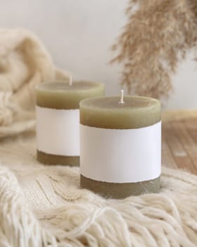Candles with label on cosy cream sweater near dry pampas grass Close up, copy space. Boho packaging mock up. Home decorations, Bohemian, ethnic or scandinavian style