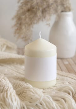 Candle with label on cosy sweater near dry pampas grass Close up, copy space. Boho packaging mock up. Home decorations, Bohemian, ethnic or scandinavian style