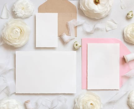 Blank cards and envelopes near cream roses and white silk ribbons top view, mockup. Romantic scene with wedding set and pastel flowers flat lay. Valentines, Spring or Mothers day concept