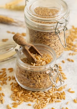 Glass jar of raw dry rye grain with a wooden spoon on white table close up. Healthy alternative low gluten seeds. Protein source for vegan and vegetarian diet.