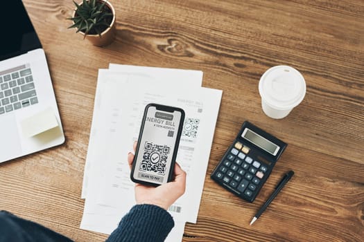 Woman scanning QR code from energy bill to make payment using fast secure payment system and smartphone code reader. Business woman paying bills using express payment technology. Female using mobile phone and laptop. Making payment. Paying bills. Paying expenses online