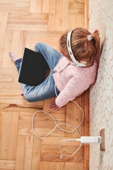 Little girl preschooler learning online solving puzzles playing educational games listetning to music and sounds using tablet and headpphones at home during pandemic quarantine