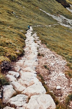 Young man with backpack hiking in a mountains, actively spending summer vacation. Rear view of teenager walking down from top of a hill to valley along mountain footpath