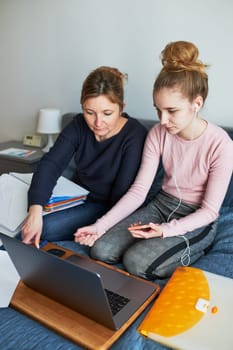 Women mother and daughter working learning remotely doing job during video chat call stream online course webinar lessons on laptop from home during COVID-19 quarantine. Women sitting on bed in front of computer looking at screen