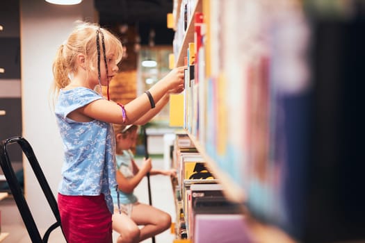 Schoolgirls looking for books in school library. Students choosing books. Elementary education. Doing homework. Learning from books. Back to school