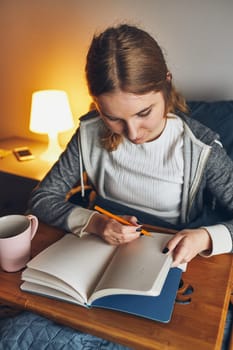 Student learning at home. Young woman making notes, reading and learning from notepad. Girl writing journal sitting in bed at home during quarantine