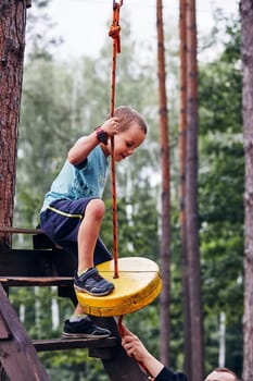 Happy boy getting in the zip line in rope park in forest while spending summer vacation. Real people, authentic situations
